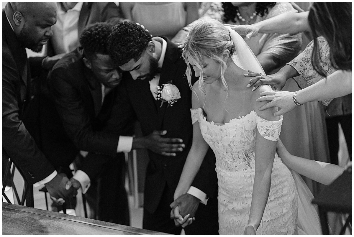 Family and friends praying over groom and bride
